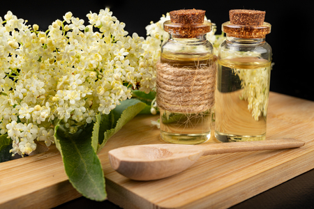 Beautiful flowers of elderberry and medicinal juice in a bottle. Natural home remedies for colds. Dark background.の写真素材