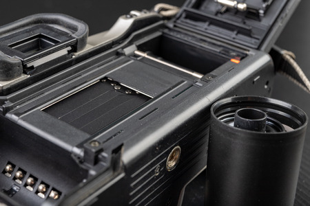 Old analog camera and black and white new film. Accessories for analog photography on a dark table. Black background.の写真素材