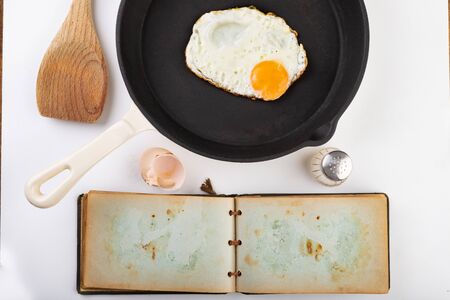 asty fried egg on a cast iron skillet. Preparing a tasty breakfast according to the recipe from an old notebook. Light background.の写真素材