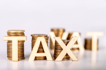 Bars stacked from coins on a white table. TAX and VAT lettering with wooden letters based on coins. White background.の写真素材
