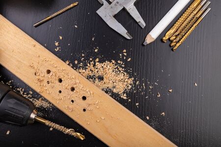 Drilling in a piece of dry planed wood. Holes made in the workshop with a screwdriver. Dark background.の写真素材
