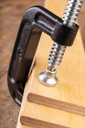 A small joinery clamp used for gluing planks. Accessories for carpenters on the workshop table. Dark background.の写真素材