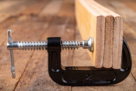 A small joinery clamp used for gluing planks. Accessories for carpenters on the workshop table. Dark...