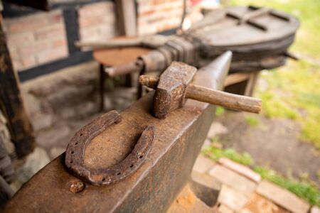 Tools in an old blacksmith's workshop. Horseshoe and hammer on a large anvil. Place - open-air museum.の写真素材