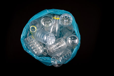 Empty plastic bottles in a garbage bag. Household waste collected in a blue bag. Dark background.