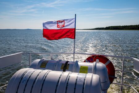 Leba, pomorskie / Polska â 14 lipca 2019 :Polish flag suspended on the stern of a small inland ship. A vessel floating on a large lake in central Europe. Season of the summer.のeditorial素材