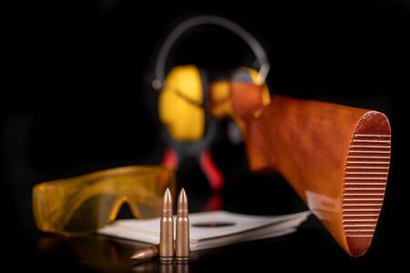 Shooting with acute ammunition at the sports shooting range. Cartridges, shield and weapon on a dark table. Black background.の写真素材