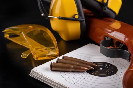 Shooting with acute ammunition at the sports shooting range. Cartridges, shield and weapon on a dark...