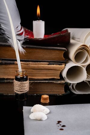 Feathers of birds for writing and calligraphy on old paper. A place for an old writer lit with candles. Dark background.の写真素材