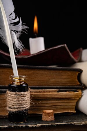 Feathers of birds for writing and calligraphy on old paper. A place for an old writer lit with candles. Dark background.の写真素材