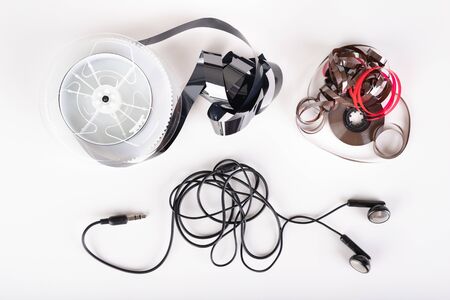 Dark headphones and magnetic tape with call recordings. Eavesdropping accessories. Light background.