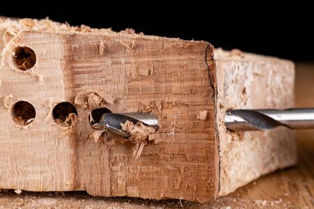 Drilling holes in raw wood. Carpentry drill in a carpentry workshop. Dark background.の写真素材