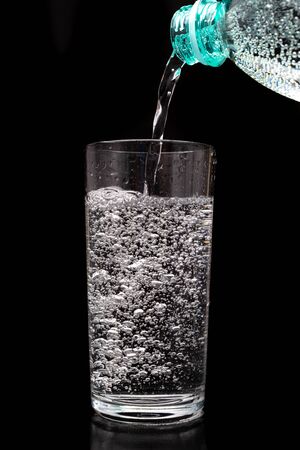 Pouring sparkling water from a bottle into a glass. Refreshing mineral water in a glass dish. Dark background.の写真素材