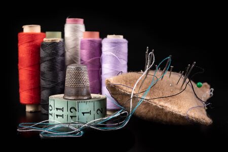 Old sewing accessories on the black table. Shears, threads and tape measure for working as a...