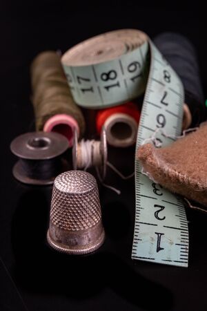 Old sewing accessories on the black table. Shears, threads and tape measure for working as a seamstress. Dark background.の写真素材