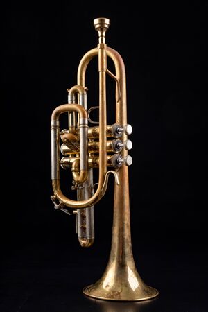 Trumpet covered with patina on a dark table. Neglected musical instrument. Black background.
