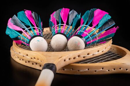Wooden badminton rackets and shuttlecocks. Accessories for team games in the hall. Dark background.