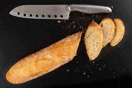 Pieces of fresh baguette and a knife on a wooden board. Delicious bread prepared to make sandwiches. Dark background.の写真素材