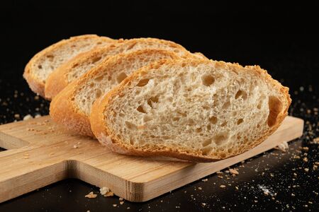 Pieces of fresh baguette on a wooden board. Delicious bread prepared to make sandwiches. Dark...