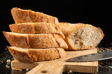Pieces of fresh baguette on a wooden board. Delicious bread prepared to make sandwiches. Dark...