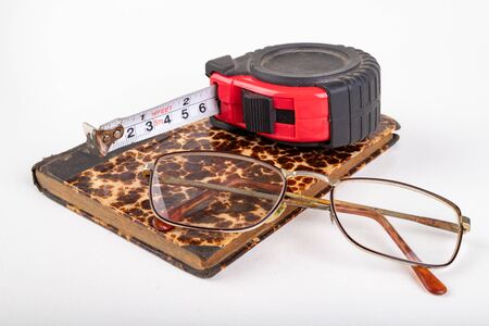 Measuring cup and old book with glasses. Accessories for measurements in carpentry. Light...