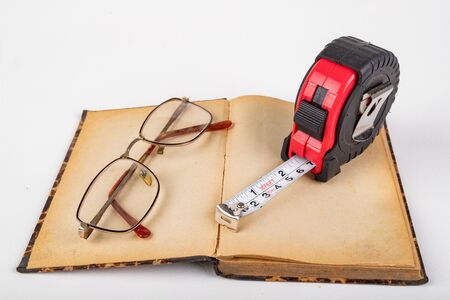 Measuring cup and old book with glasses. Accessories for measurements in carpentry. Light background.の写真素材