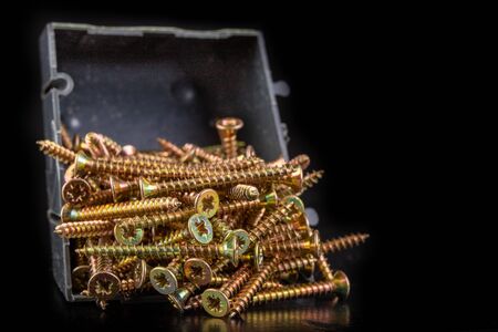 Carpentry screws in a plastic container. Furniture accessories in the workshop. Dark background.の写真素材