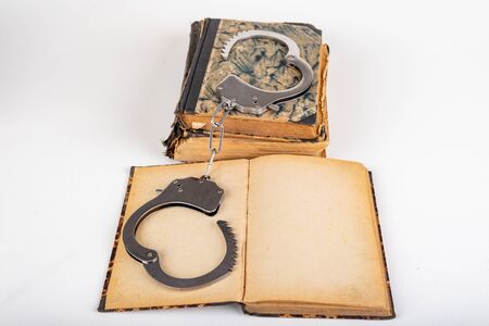 Old books and metal handcuffs. Literature and prison for bad words. Light background.