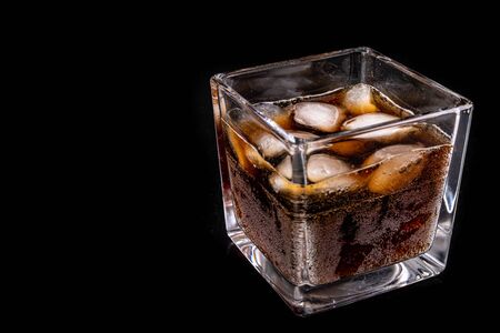 A cold refreshing drink with ice in a glass. Ice cubes and a sweet cold drink in a glass dish. Dark...