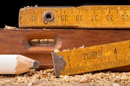 Carpentry measure, spirit level and pencil in sawdust on wooden table. Small carpentry work in a home workshop. Dark background.の写真素材