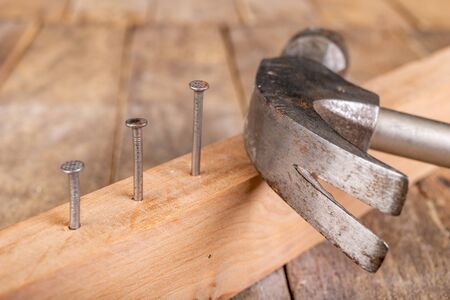 Carpenter's hammer and steel nails on a wooden workshop table. Small carpentry work in the workshop. Dark background.の写真素材