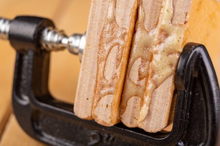 Glued pieces of wood and carpentry clamp on a wooden table. Carpentry accessories in a wood workshop. Dark background.の写真素材