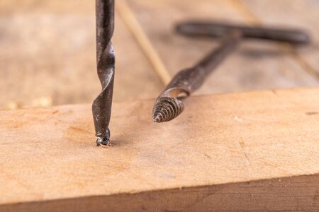 Manual drill for making holes in wood. Carpentry tools on a workshop table. Dark background.