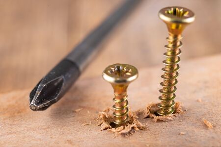 Screwdriver and screws for connecting wooden elements. Carpentry tools on a workshop table. Dark...