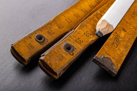 Carpentry measure and white pencil on a dark table. Tools needed to work in a carpentry shop. Dark background.の写真素材