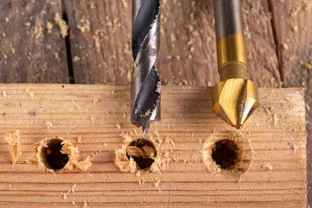 Drilling holes in a piece of wood. Countersinking the hole for wood screws. Dark background.