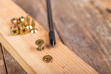 Wood screws and a screwdriver on a piece of wood. Carpentry work in a home workshop. Dark background.の写真素材