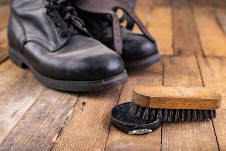 Polishing of military boots on a wooden table. Maintenance and protection of leather shoes. Dark...