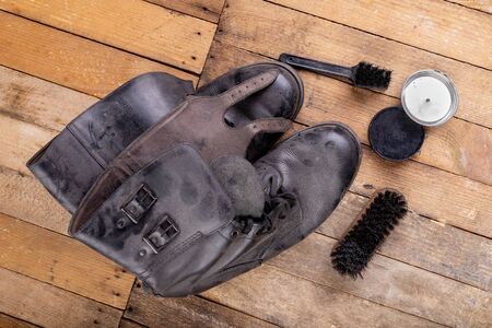 Polishing of military boots on a wooden table. Maintenance and protection of leather shoes. Dark...