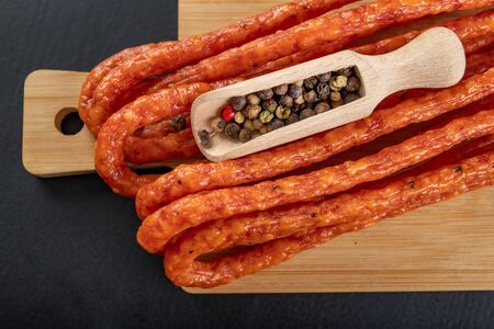 Tasty pepper kabanos. Meat snack for a home party. Dark background.