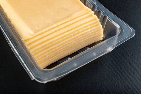 Slices of yellow cheese in a plastic package. Food from the market on the kitchen table. Dark...