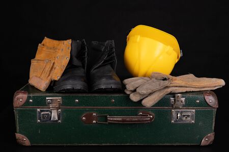 Protective clothing and an old suitcase. Economic emigration of production workers. Dark background.