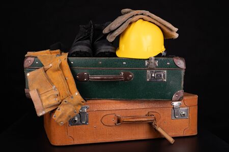 Protective clothing and an old suitcase. Economic emigration of production workers. Dark background.