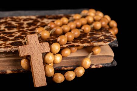 Wooden rosary arranged on an old book. Accessories for prayer in a Christian church. Dark...
