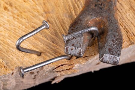 Extracting old nails from a piece of raw wood. Carpentry work in the workshop. Dark background.