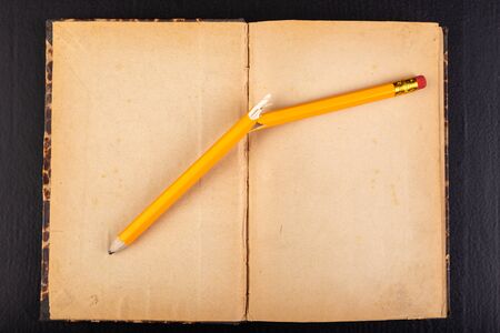 A broken pencil and an old book. Emotions during office work. Dark background.
