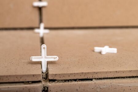 Plastic crosses that position the tiles when laying. The process of sticking porcelain tiles. Light background.の写真素材