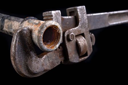 Old dirty pipe and hydraulic wrench. Accessories and tools for a plumber. Dark background.