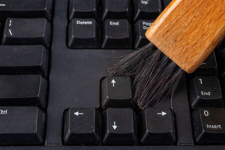 Cleaning the keyboard from dust and dirt with a brush. Maintenance and cleaning of computer hardware. Dark background.の写真素材