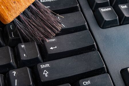 Cleaning the keyboard from dust and dirt with a brush. Maintenance and cleaning of computer hardware. Dark background.の写真素材